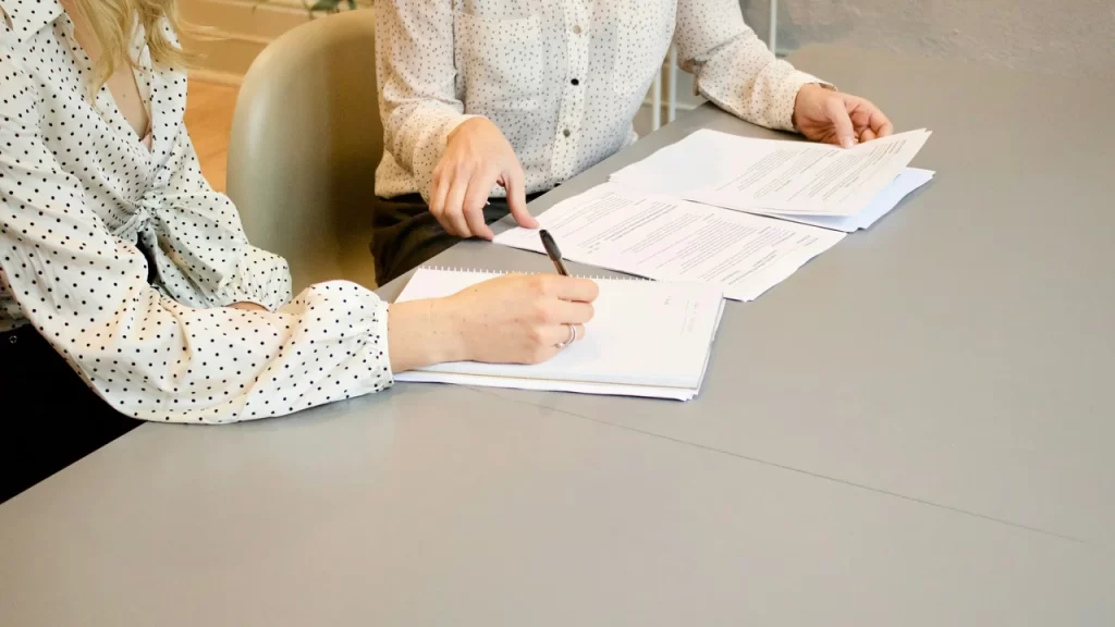 Two professionals reviewing and signing documents, representing a letter of support for visa application and official immigration paperwork.