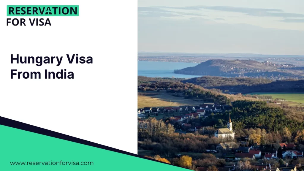 An elevated view of a peaceful Hungarian village nestled among rolling hills near a large body of water, featuring a prominent white church with a spire.