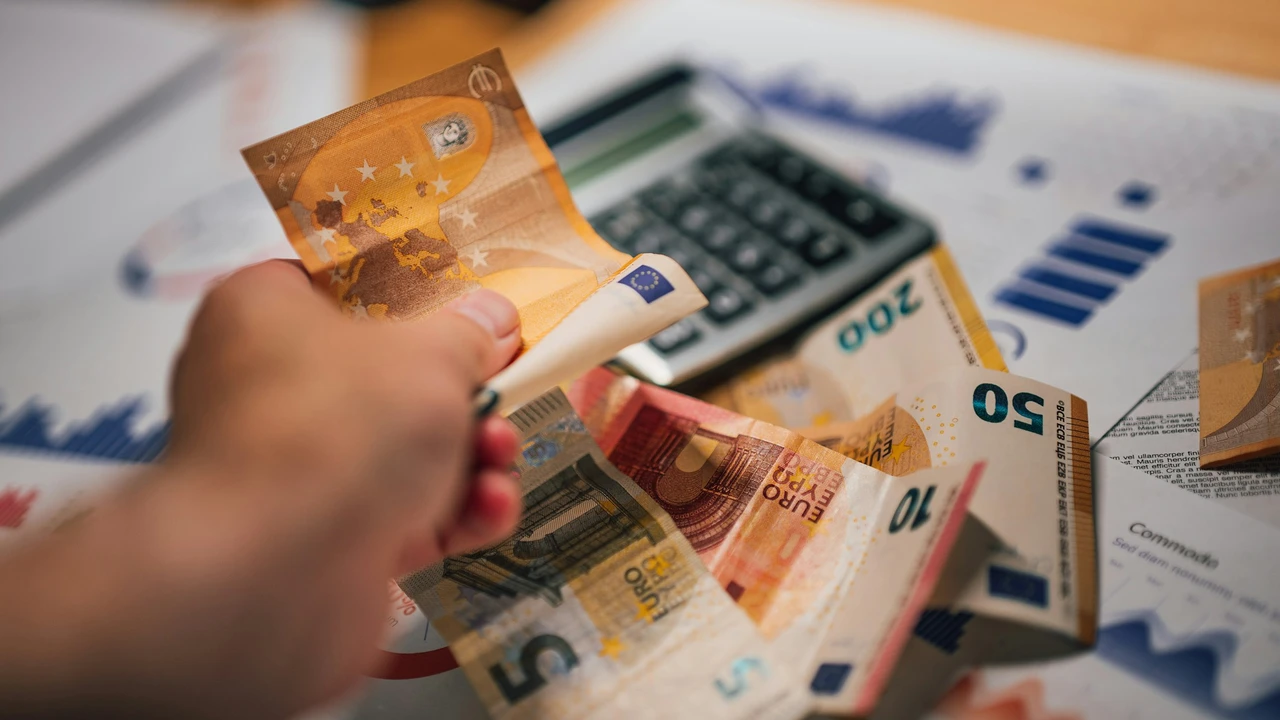 Hand holding euro banknotes over financial documents and calculator, representing budgeting, expense tracking, personal finance, and money management.