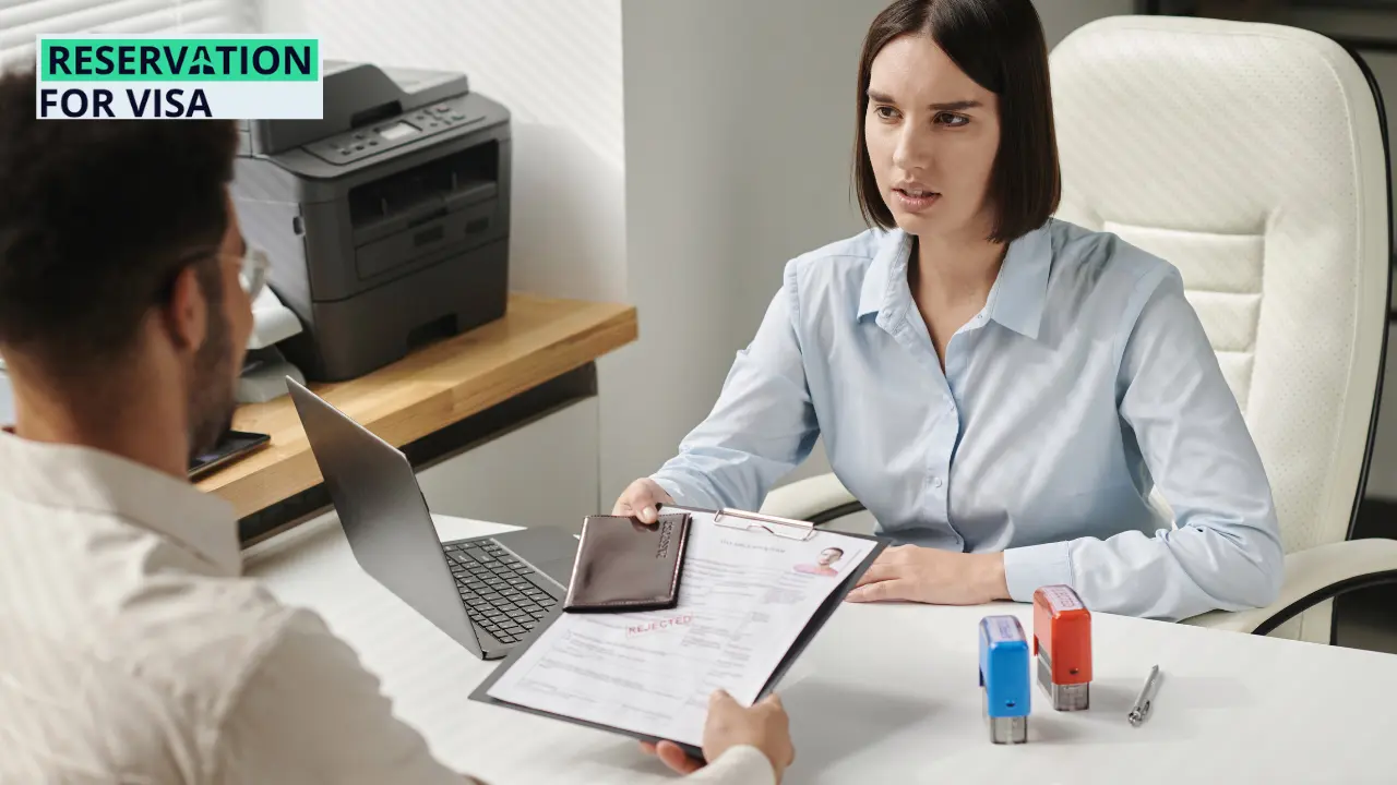 A woman at a desk appears to be discussing a visa application with a man holding a rejected form and passport, symbolizing common visa rejection reasons during the visa interview or processing stage, with the Reservation for Visa logo visible in the corner.